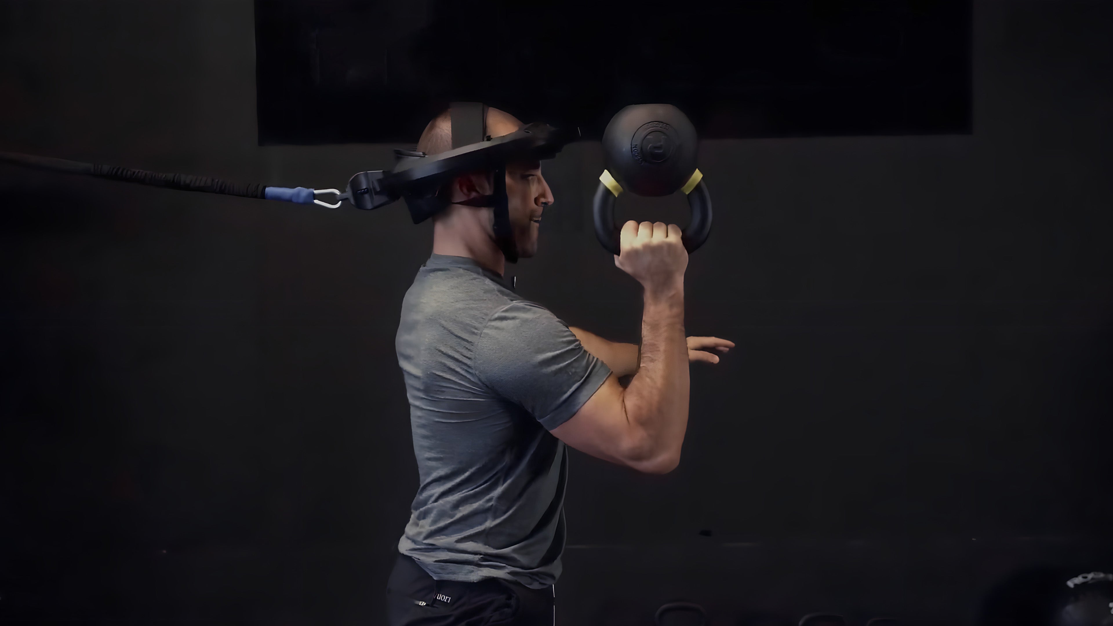 Mike Salemi wears Iron Neck on his head and holds a kettlebell in his hand.
